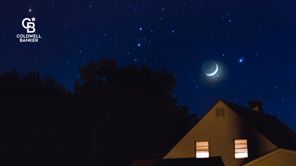 Home at night with lit windows under a crescent moon.
